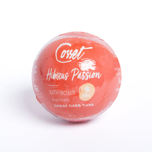 Round, red Hibiscus Passion bath bomb in clear plastic wrap with white text detailing Ylang Ylang and Clove Leaf ingredients.